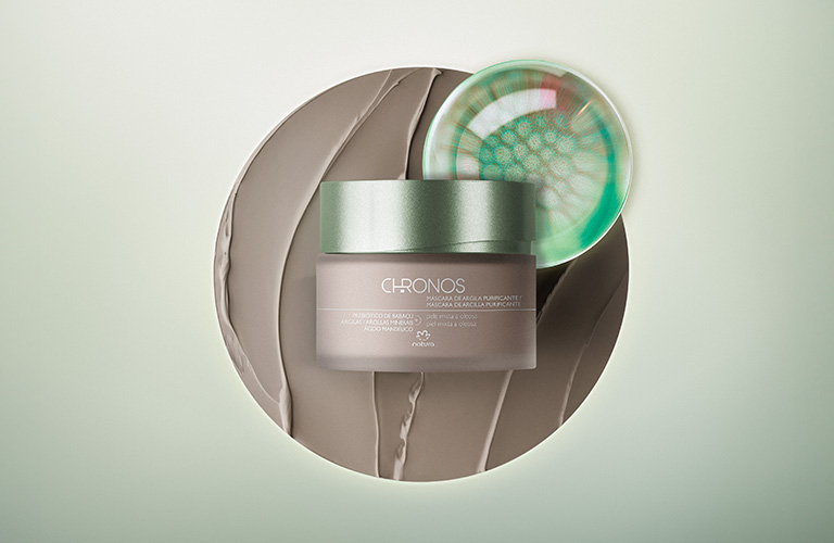 Foto con fondo claro, bote de mascarilla facial Chronos sobre base marrón texturizada y detalle de vidrio verde.